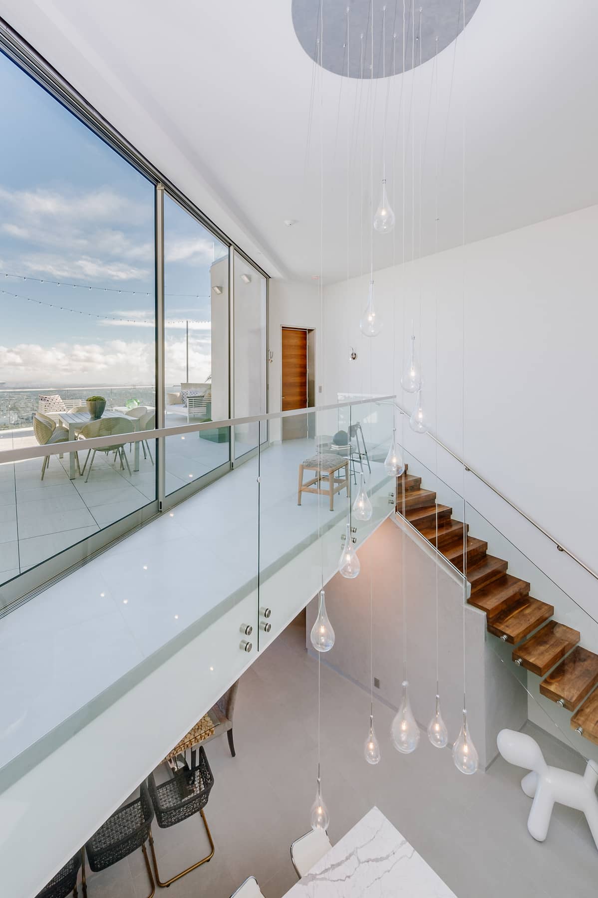 Double-height interior with suspended lights, glass bridge and wood stair at 8693 Franklin